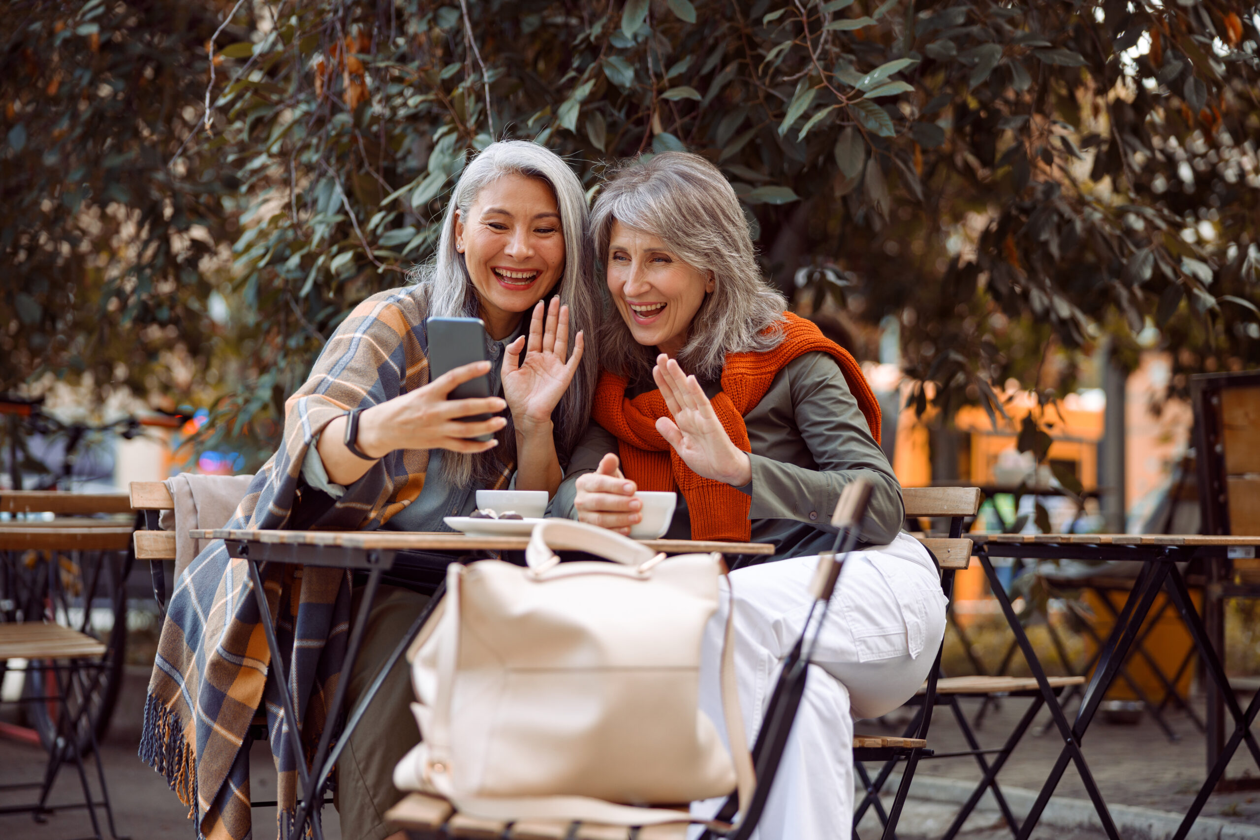 Senior women having tea and getting a selfie at an outdoor coffee shop